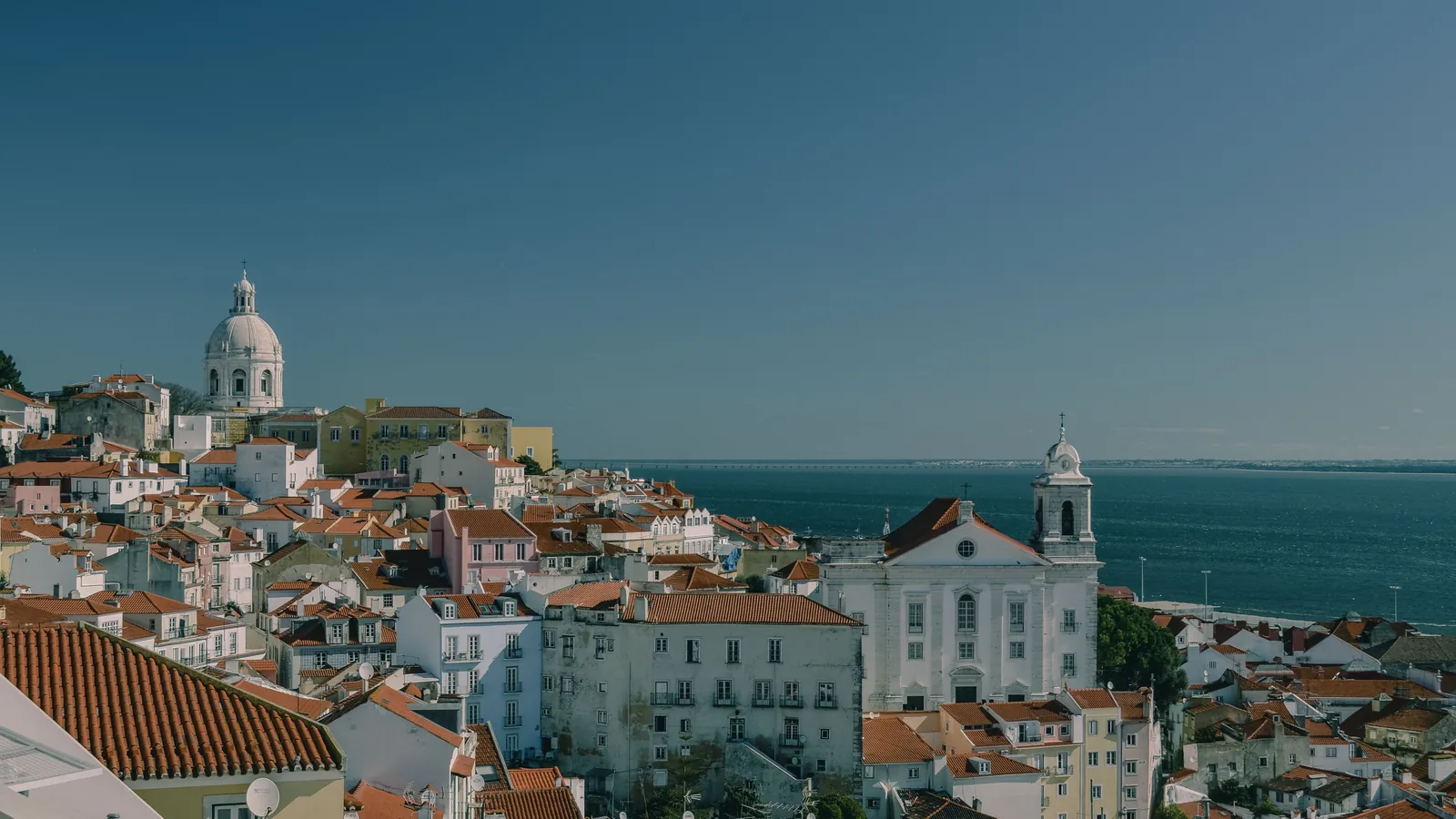 Alfama’s red-tiled rooftops and churches overlooking the Tagus River in Lisbon