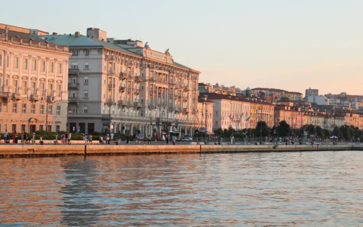 Historic waterfront buildings in Trieste reflected in the water at sunset