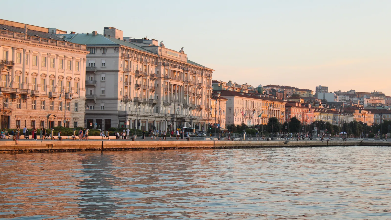 Historic waterfront buildings in Trieste reflected in the water at sunset